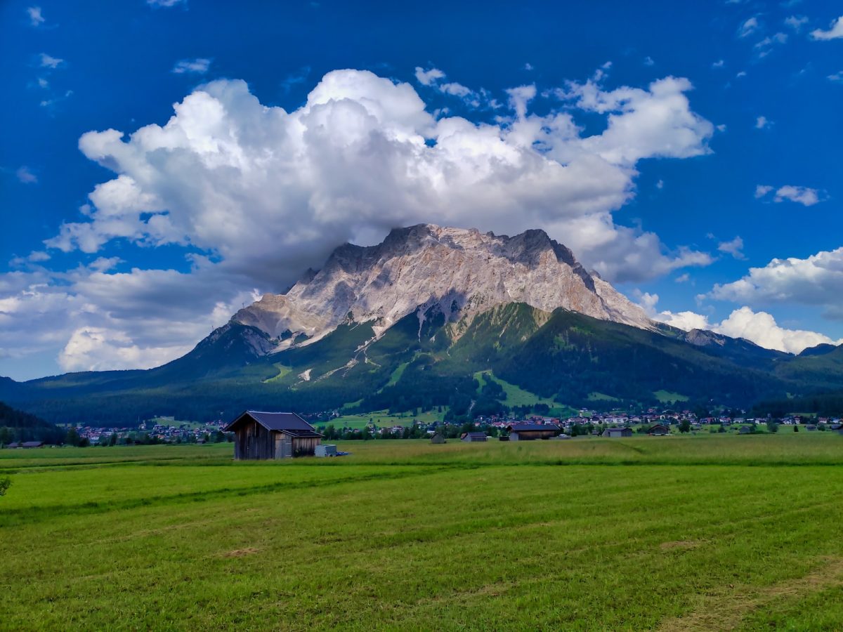 brown wooden house on green grass field near mountain under white clouds and blue sky during